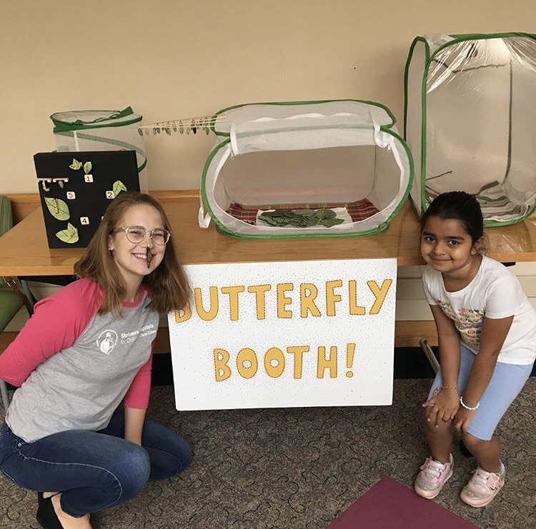 Nora and a young butterfly enthusiast pose with monarchs in front of the Butterfly Booth