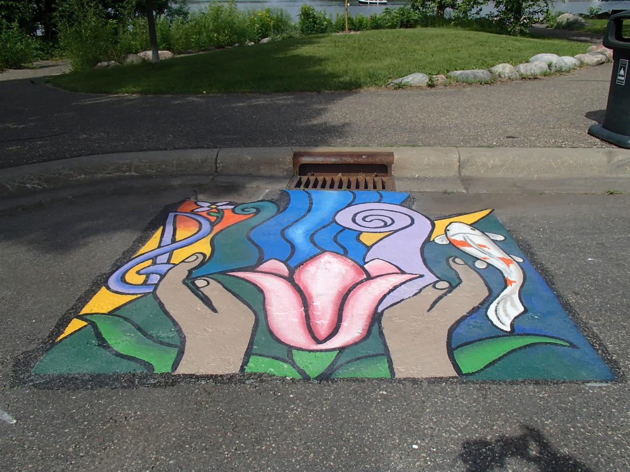 Storm drain mural contains music and fish to connect it to como park and hands representing our responsibliity to care for the lake